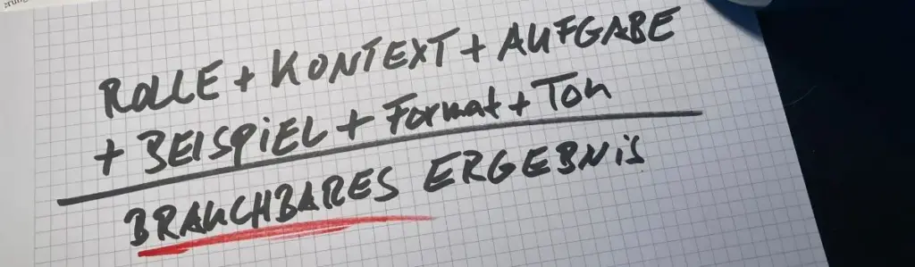 Handgeschriebene Notiz auf kariertem Papier mit den Worten: 'Rolle + Kontext + Aufgabe + Beispiel + Format + Ton = Brauchbares Ergebnis'. Umgeben von einer Tasse, gelbem Notizblock und Papieren auf einem dunklen Tisch.
